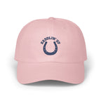 A pink baseball cap featuring a navy blue embroidered horseshoe and the text SADDLIN' UP.