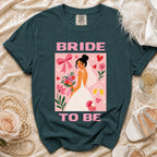 Teal t-shirt with "BRIDE TO BE" text and bride graphic on a pink background.