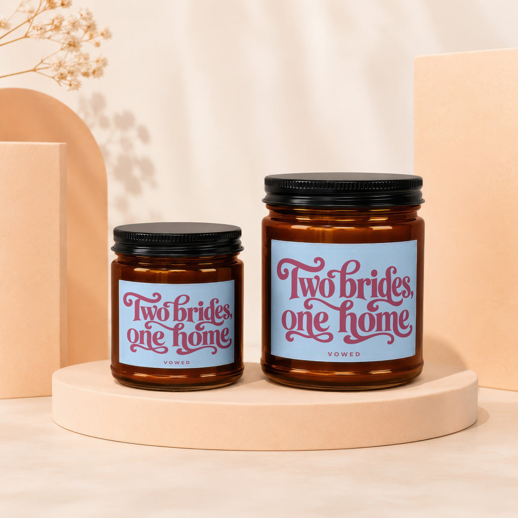 Two amber glass candles with black lids and "Two brides, one home" labels.