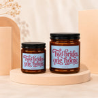 Two amber glass candles with black lids and "Two brides, one home" labels.