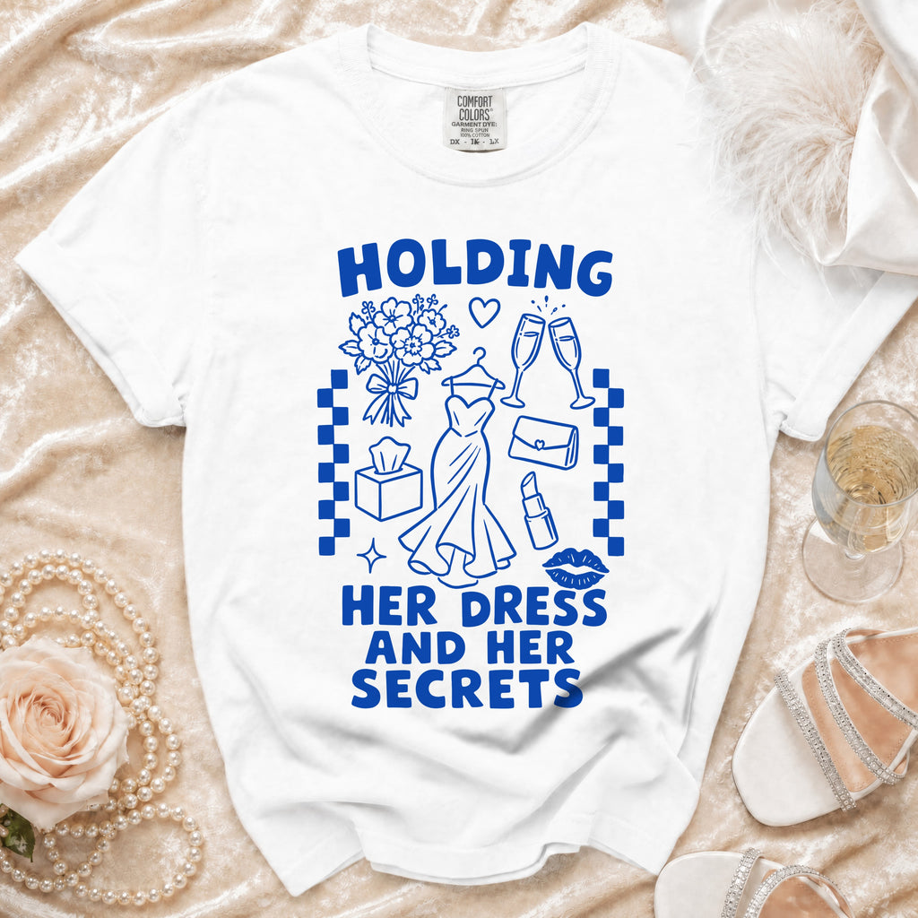 White t-shirt with blue text and graphics: "HOLDING HER DRESS AND HER SECRETS".
