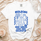 White t-shirt with blue text and graphics: "HOLDING HER DRESS AND HER SECRETS".