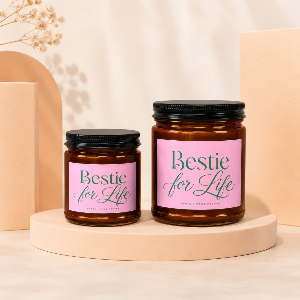 Two amber glass candles with pink labels reading "Bestie for Life" and "Vowed | Hand Poured".