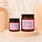 Two amber glass candles with pink labels reading "Bestie for Life" and "Vowed | Hand Poured".