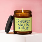Amber glass candle with lit flame, lid ajar, features text "Forever starts today Vowed".