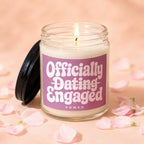 Glass jar candle with a lit wick, labeled "Officially Dating Engaged Vowed."