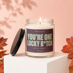 Scented candle in glass jar with label reading "YOU'RE ONE LUCKY B*TCH AND HE KNOWS IT".
