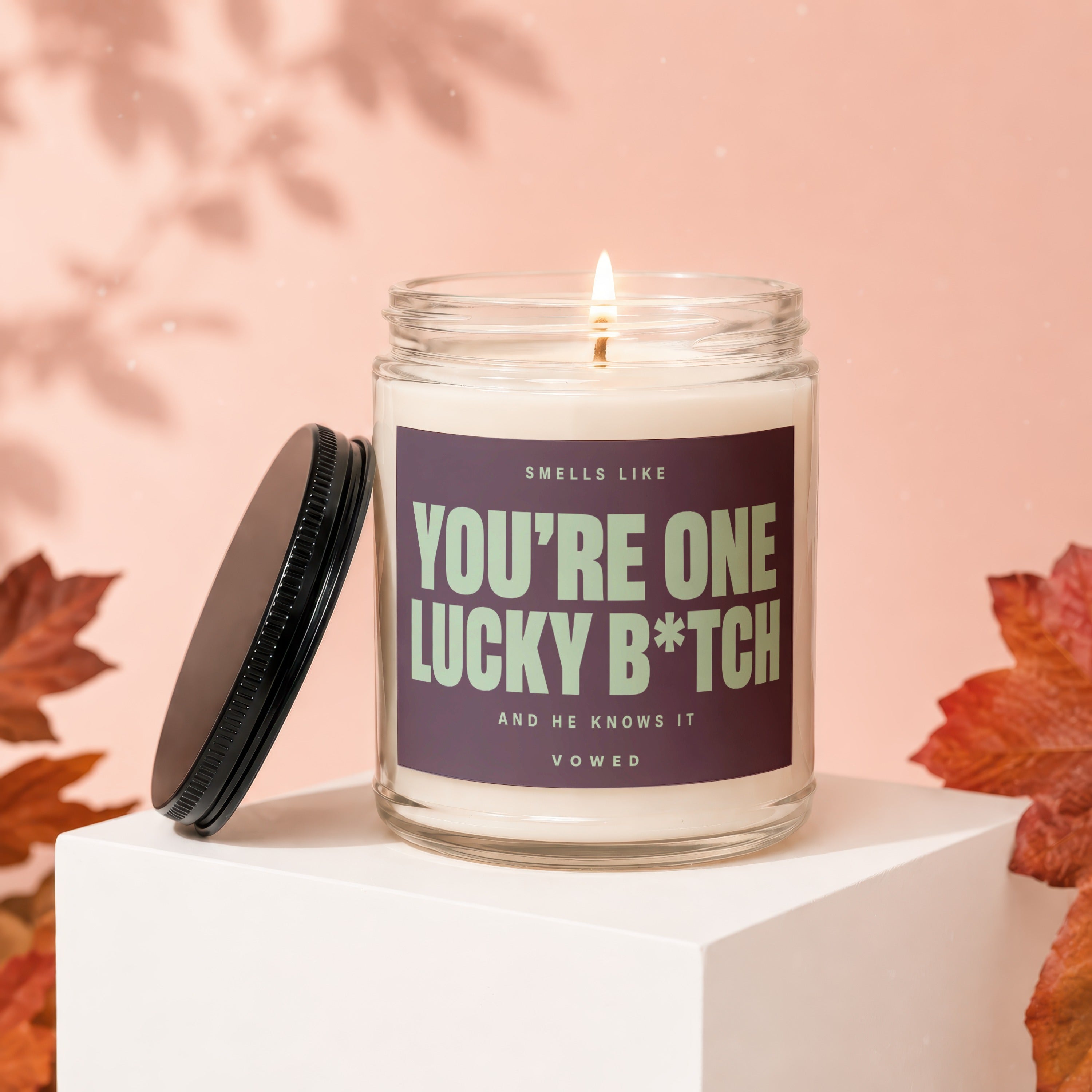 Scented candle in glass jar with label reading "YOU'RE ONE LUCKY B*TCH AND HE KNOWS IT".