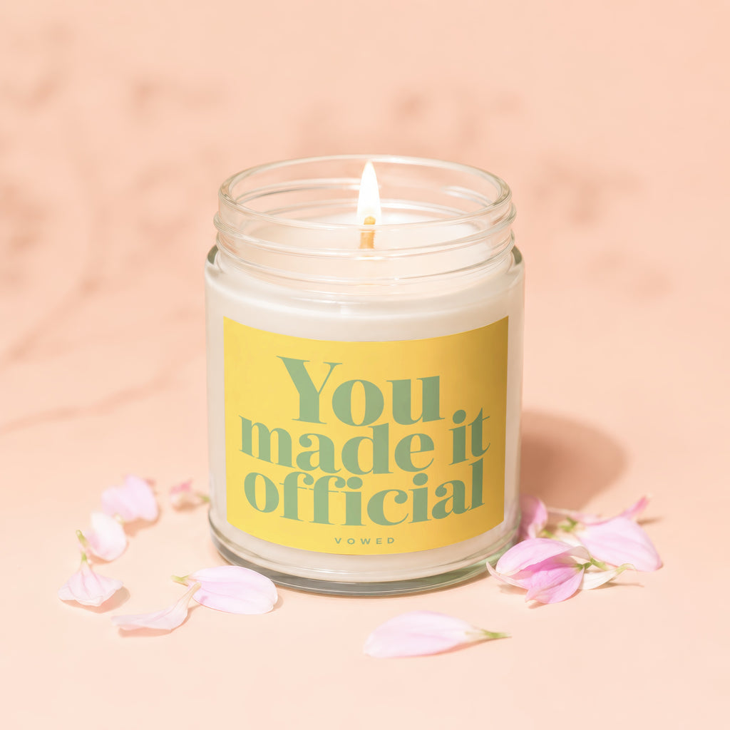 Candle with yellow label reading "You made it official" with pink petals.