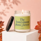 Lit candle in a glass jar with a black lid, displaying "The honeymoon phase, forever" text.