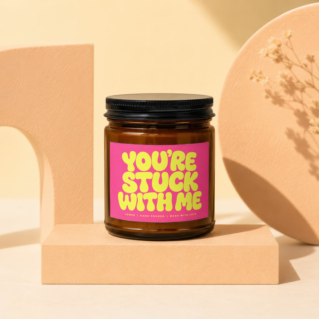 Amber glass candle with "YOU'RE STUCK WITH ME" text on pink label.