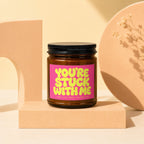 Amber glass candle with "YOU'RE STUCK WITH ME" text on pink label.
