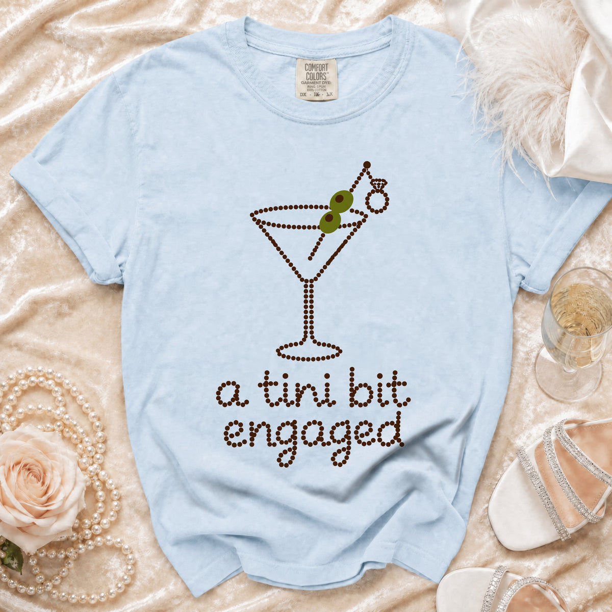 Light blue t-shirt with a rhinestone martini glass graphic and text "a tini bit engaged".