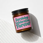 Glass candle with pink label reading "Surviving Celebrating Forever VOWED".