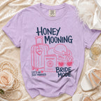 Purple t-shirt with "Honey Mooning Bride Mode" graphic, suitcase, passport, and hat.