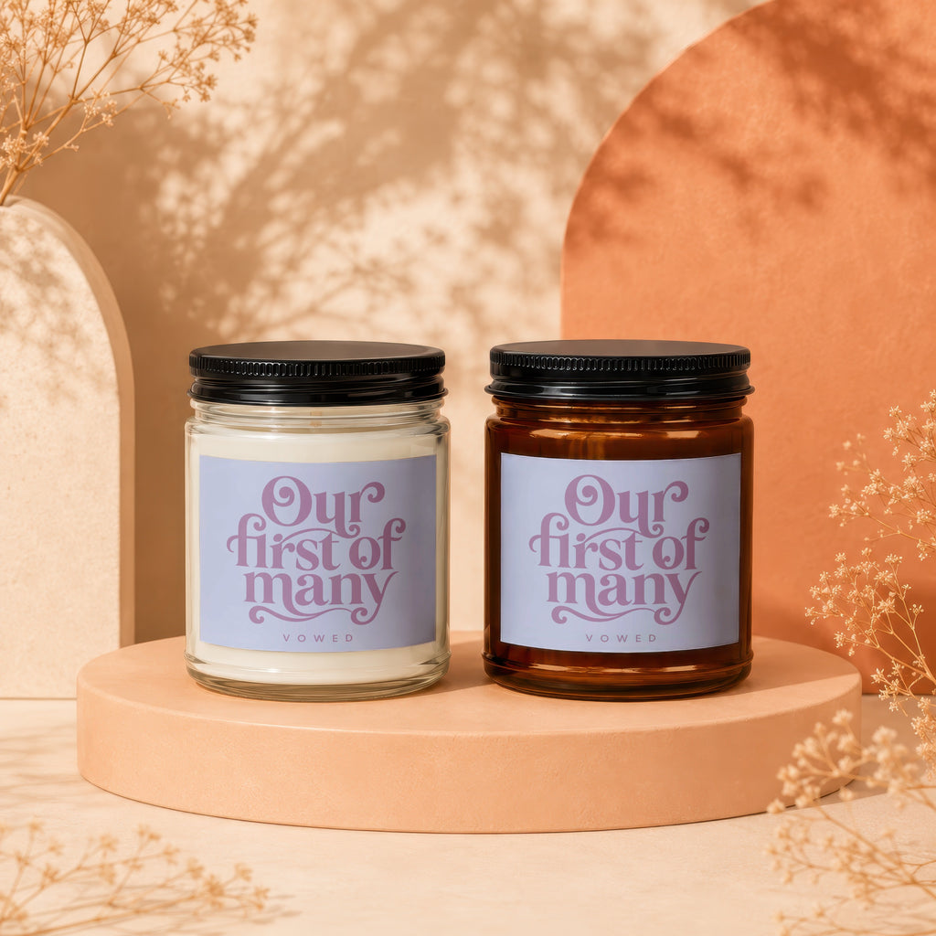 Two glass jar candles with black lids, displaying "Our first of many" text.