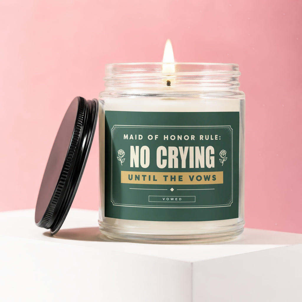 Glass candle with burning wick, black lid, and label reading "Maid of Honor Rule: No Crying Until the Vows".