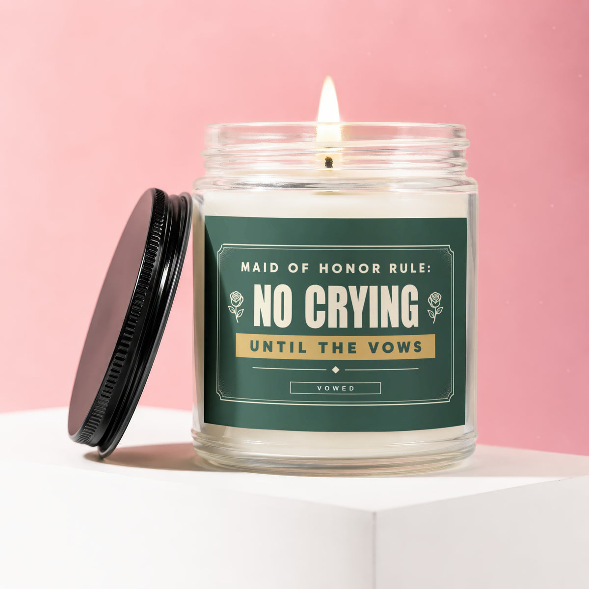 Glass candle with burning wick, black lid, and label reading "Maid of Honor Rule: No Crying Until the Vows".