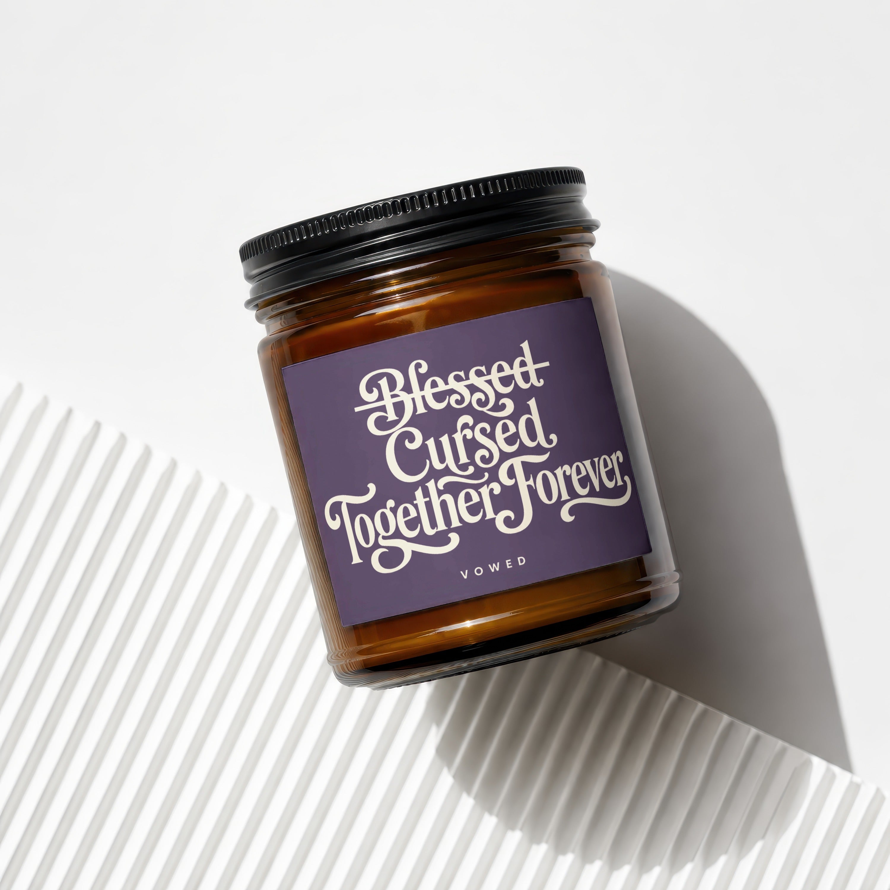 Amber jar candle with "Blessed Cursed Together Forever" text and "vowed" on purple label.