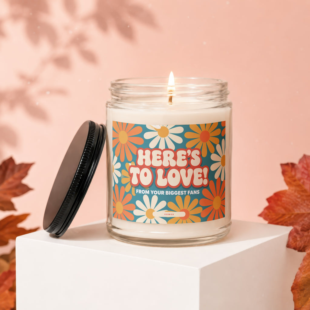 Candle with "HERE'S TO LOVE!" text and floral design on a pink background.