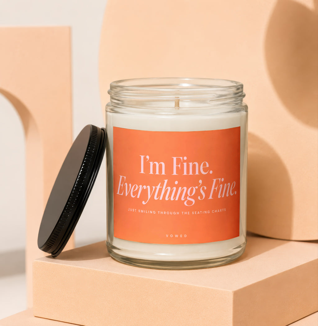 Glass candle with orange label reading "I'm Fine. Everything's Fine. Just Smiling Through The Seating Charts. VOWED."