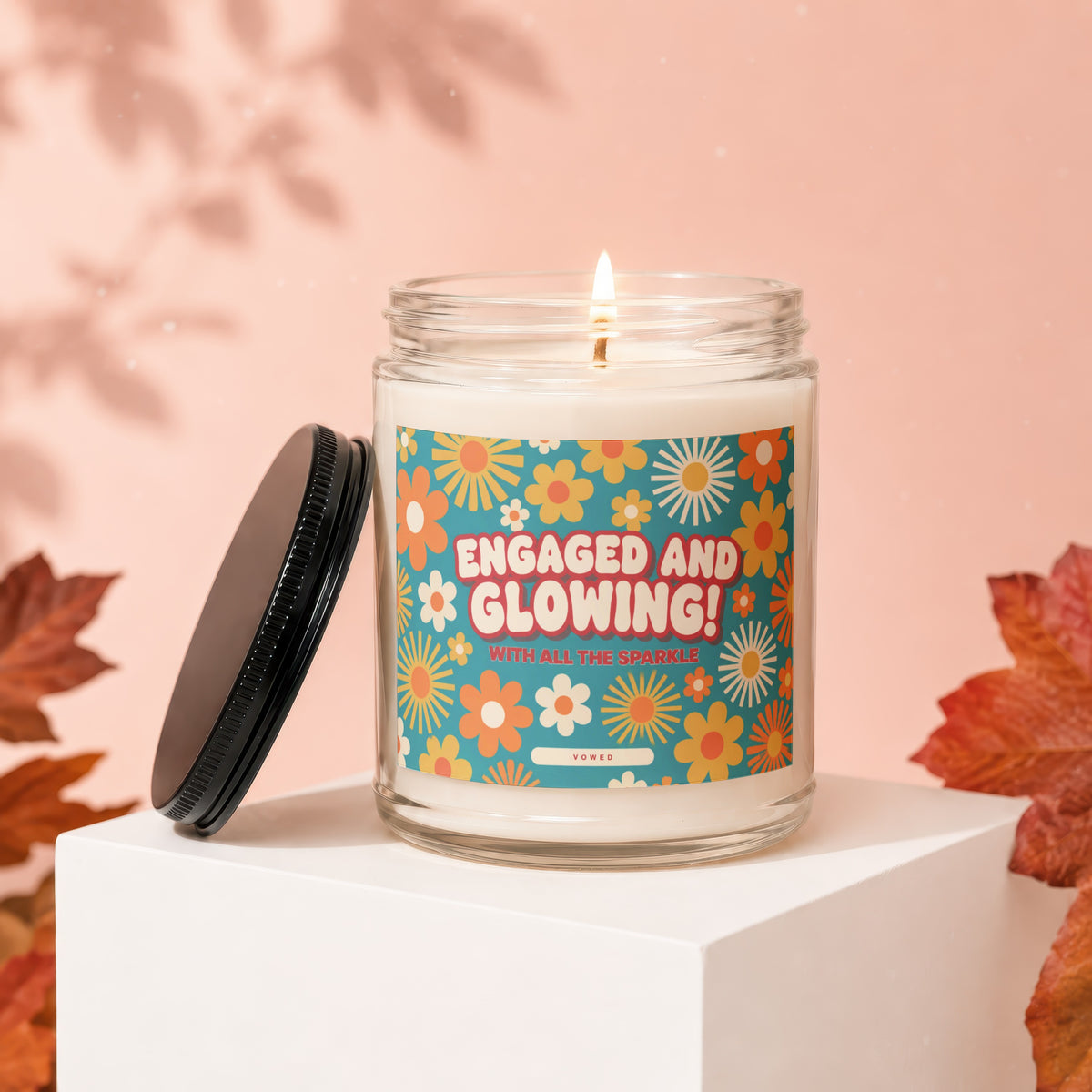 Candle with "Engaged and Glowing" text on a floral label, lid beside it.
