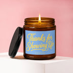 Amber jar candle with lit flame and blue label reading "Thanks for Showing Up VOWED".