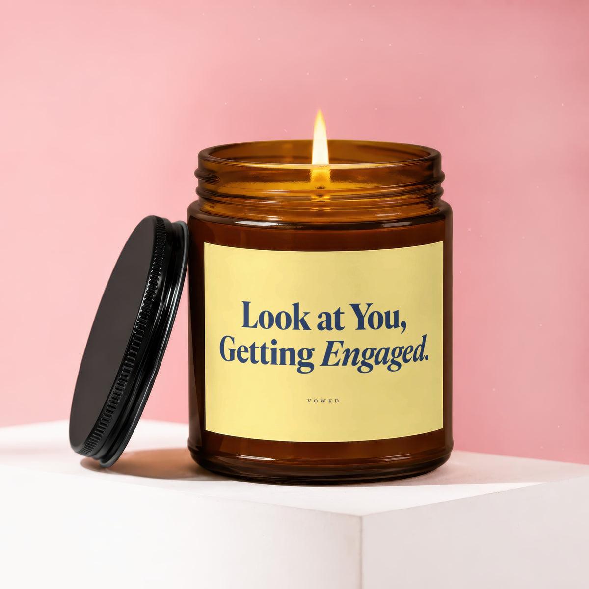 Amber jar candle with a lit wick, lid off, reading "Look at You, Getting Engaged."