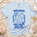 Light blue t-shirt with blue graphic text "HOLDING HER DRESS AND HER SECRETS".