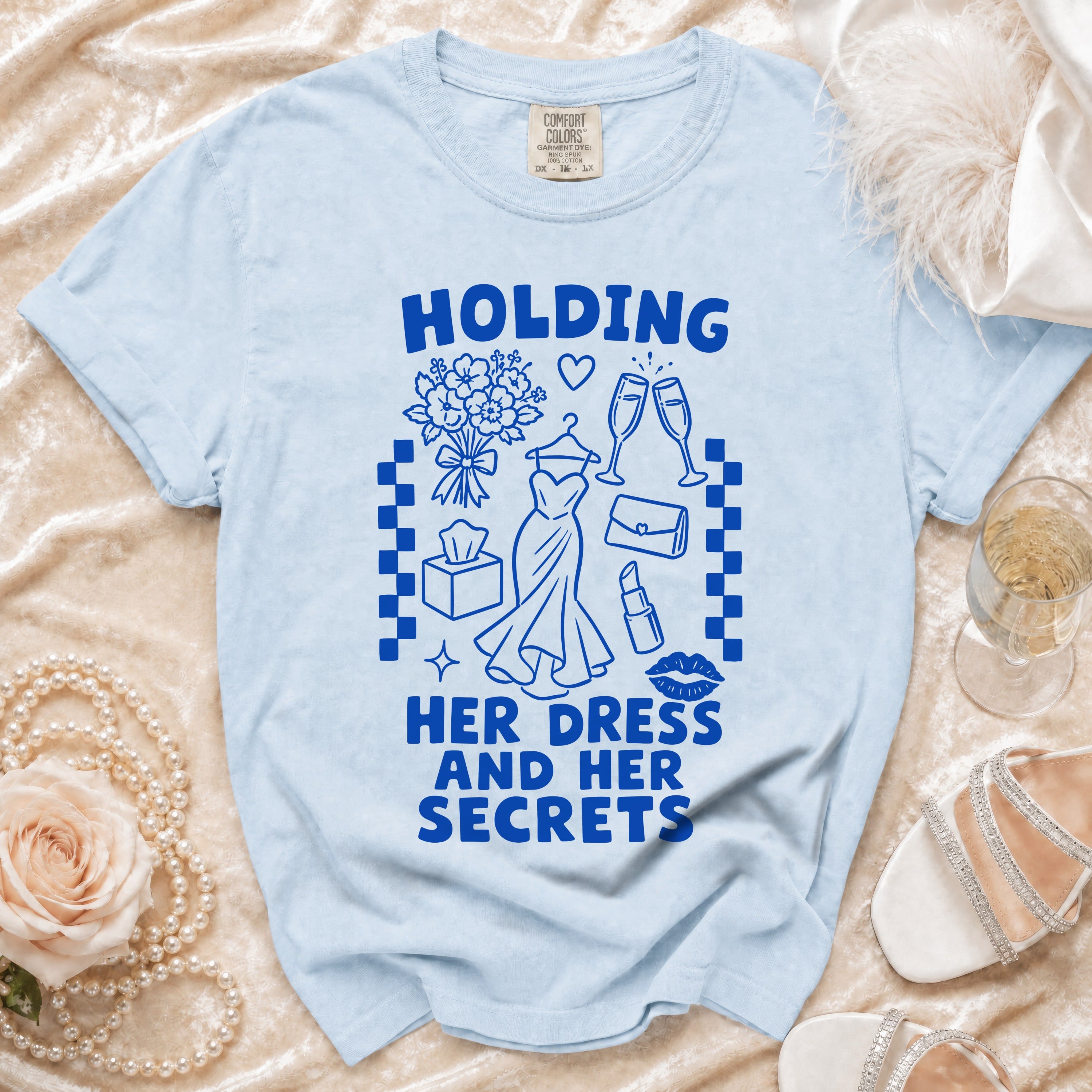 Light blue t-shirt with blue graphic text "HOLDING HER DRESS AND HER SECRETS".