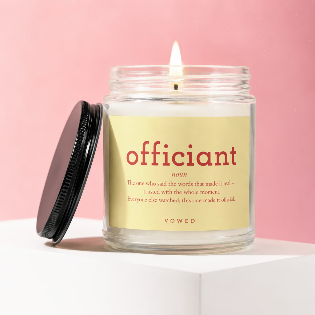 Glass candle with "officiant" definition label and lit flame on a pink background.