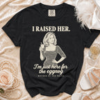 A black t-shirt printed with retro-style graphics, holding a glass and text reading I raised her. I am just here for the eggnog. Mother of the bride.