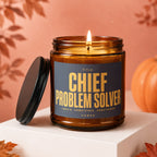 Amber candle with "Chief Problem Solver" label and lit wick.