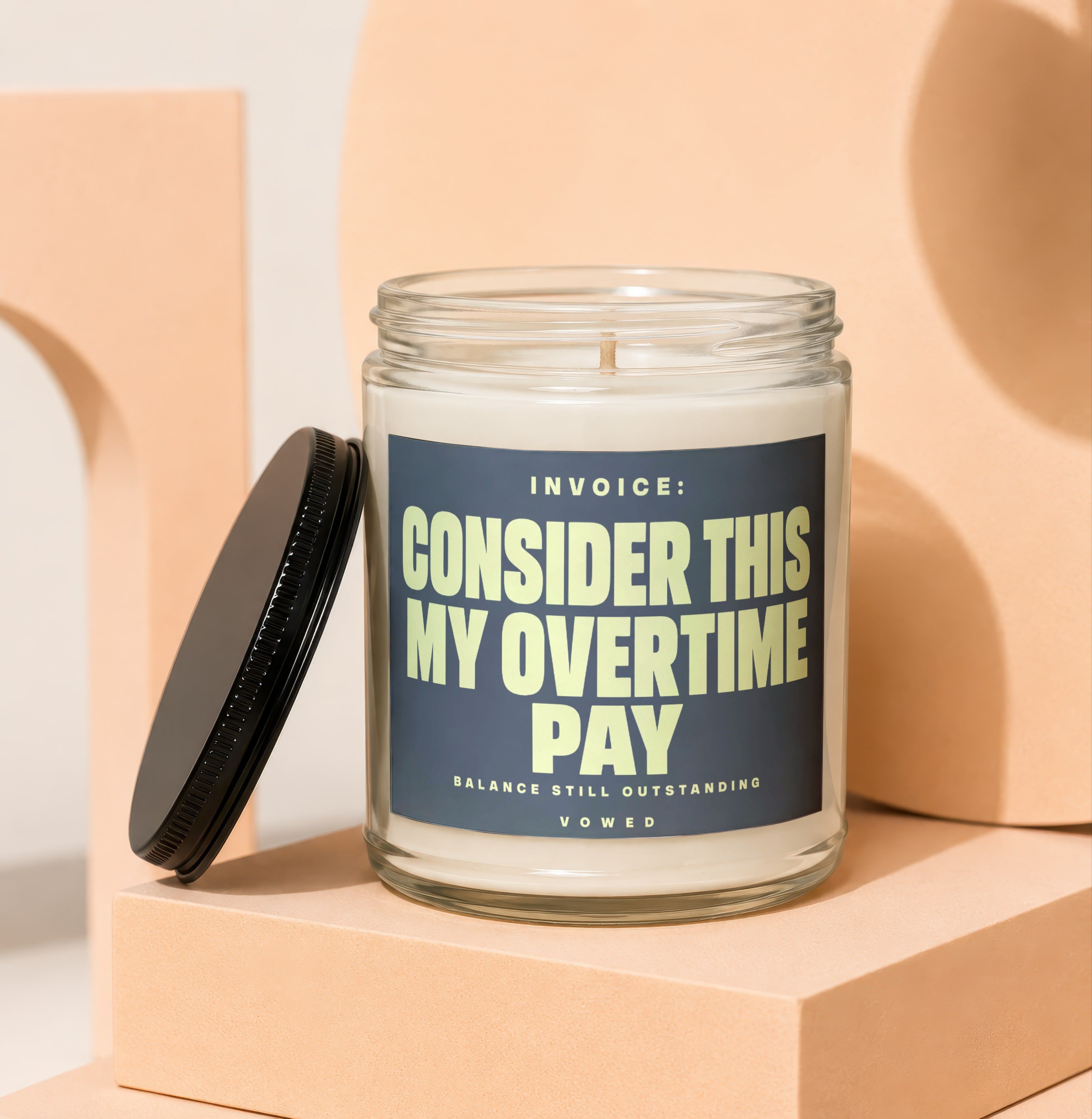 Glass jar candle with black lid, labeled "Invoice: Consider This My Overtime Pay."