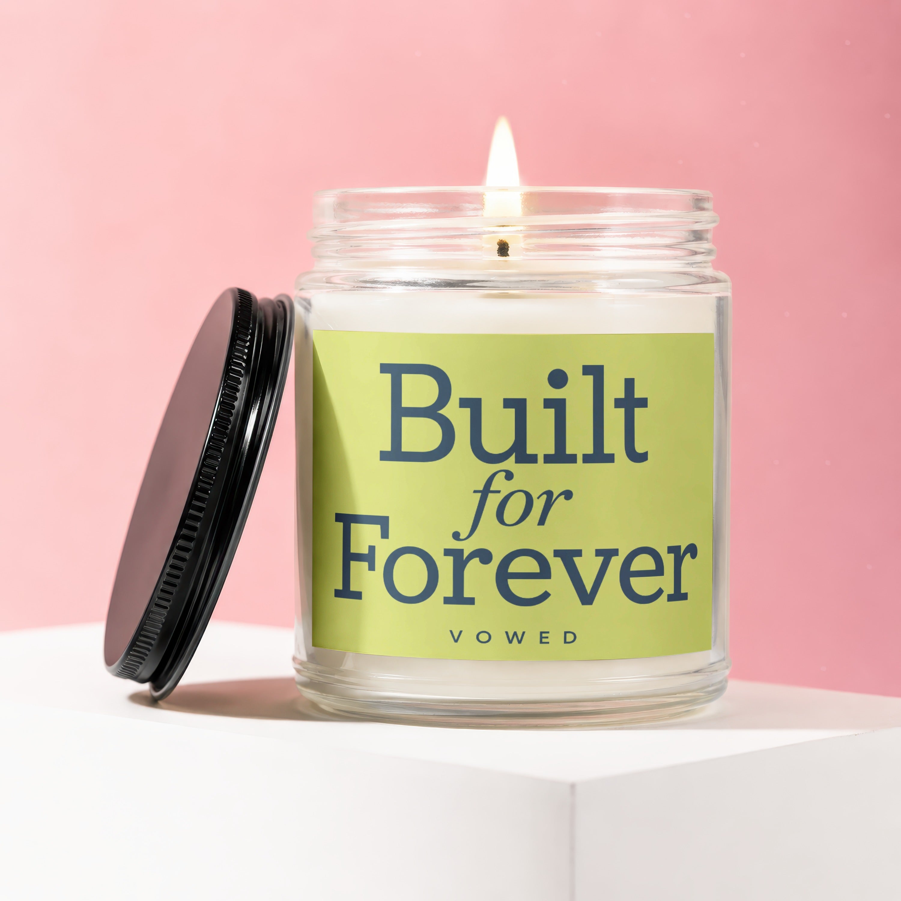 Glass candle with lit wick, featuring "Built for Forever" text on a green label.