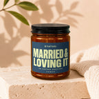 Amber jar candle with dark lid, labeled "STATUS: MARRIED & LOVING IT".