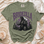 Olive green t-shirt with "Bridezilla" text, Godzilla wearing a veil and sunglasses, holding flowers.