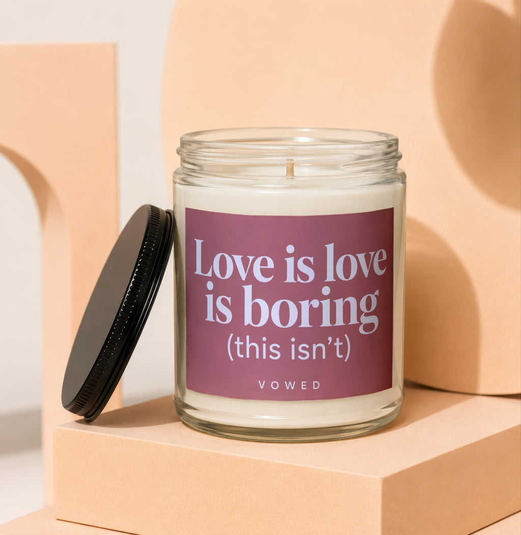 Glass jar candle with maroon label reading "Love is love is boring (this isn't)".