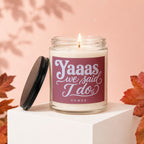 Scented candle with "Yaaas we said I do" text, lid off, with autumn leaves.