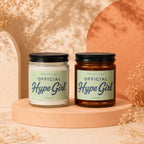 Two candles labeled "Smells Like Official Hype Girl" on a display stand.