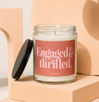Glass candle with "Engaged & Thrilled" and "VOWED" text on pink label.