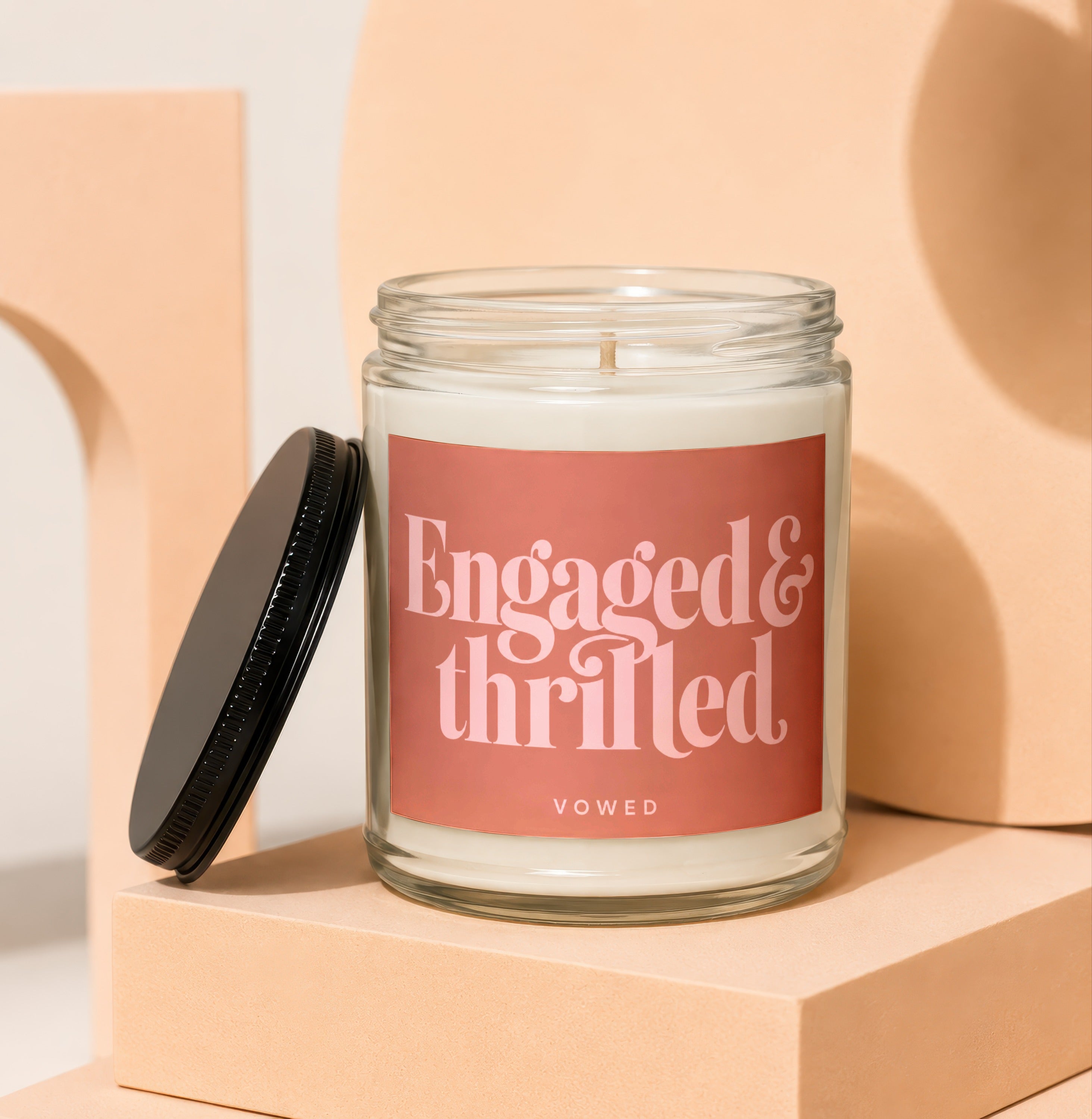 Glass candle with "Engaged & Thrilled" and "VOWED" text on pink label.