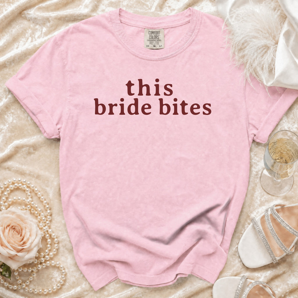 Pink t-shirt with "this bride bites" text, pearls, rose, and champagne.