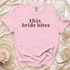 Pink t-shirt with "this bride bites" text, pearls, rose, and champagne.