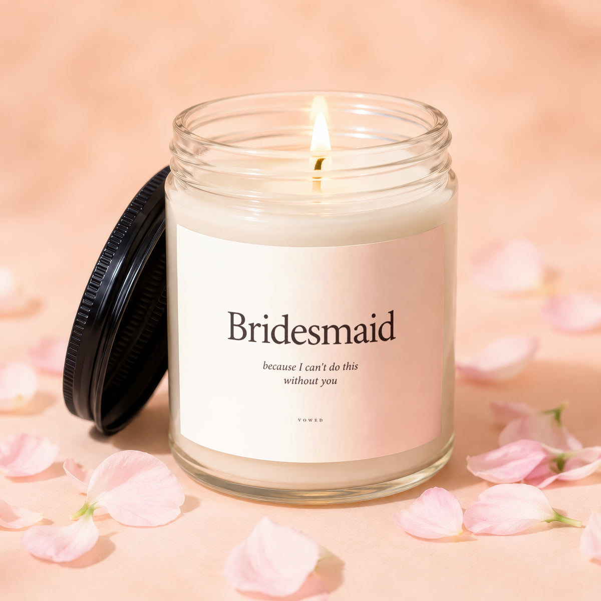 Bridesmaid candle with lid off and flame lit, surrounded by pink petals.