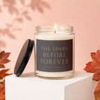Candle with "The Spark Before Forever" text, lid off, surrounded by autumn leaves.