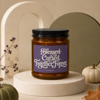 Amber jar candle with purple label that reads "Blessed Cursed Together Forever Vowed".