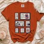Orange Comfort Colors t-shirt with Halloween-themed stamps including a ghost, coffin, haunted house, and skeletons.