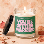 Candle with lit wick and green label that reads "Smells like You're Getting Married".