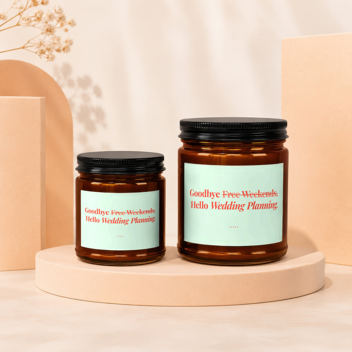 Two amber glass candles with black lids and light blue labels reading "Goodbye Free Weekends, Hello Wedding Planning."